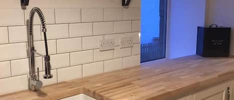 A modern kitchen with a wooden countertop, white cabinetry, a built-in sink, and a window above the sink.