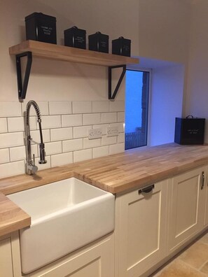 A modern kitchen with a wooden countertop, white cabinetry, a built-in sink, and a window above the sink.