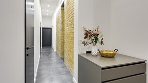 Un couloir moderne avec un mur d’accent en briques, un comptoir d’accueil agrémenté d’un vase et d’un panier, et une porte au fond.