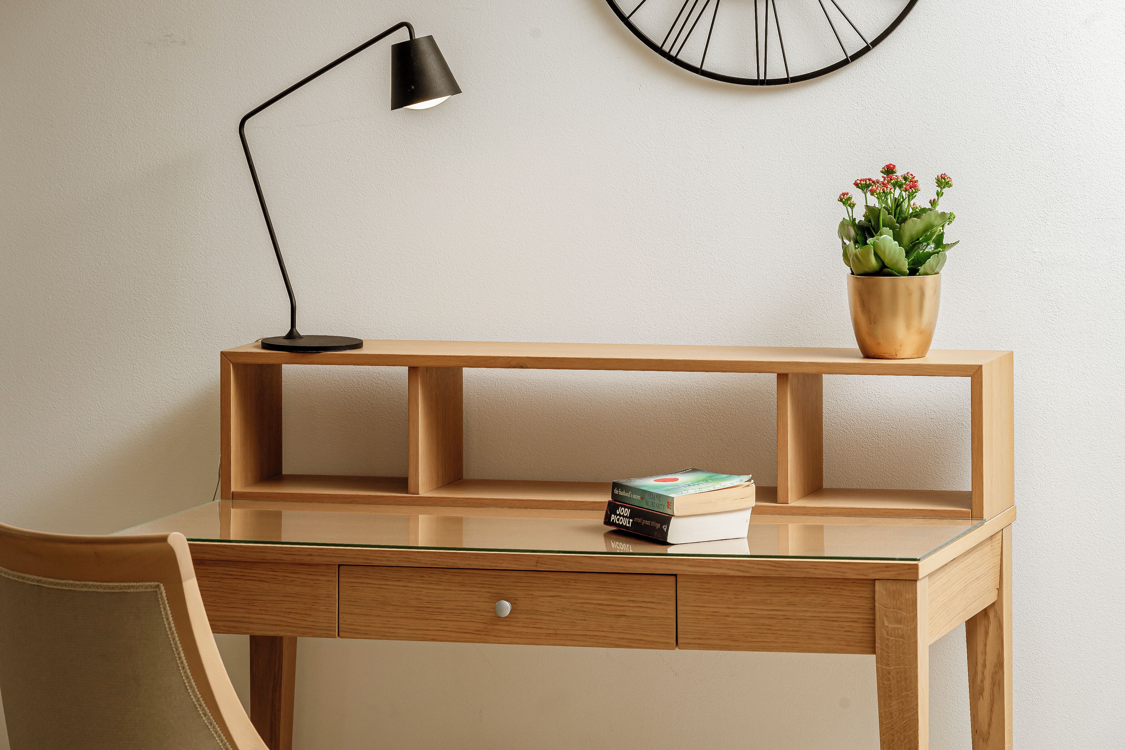 A wooden desk with a glass top, a black desk lamp, a potted plant, and a few books.