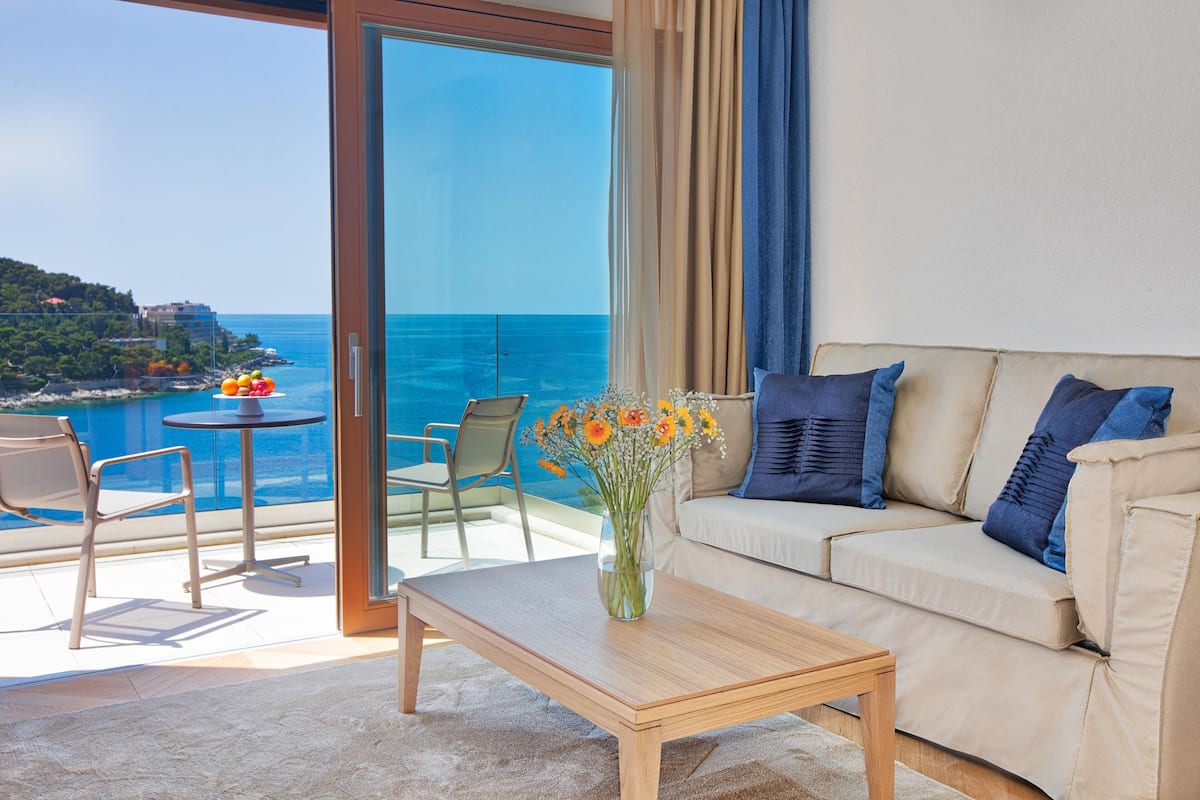 A balcony with a view of the sea, a sofa, a table, and a vase with flowers.