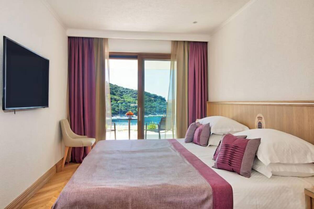 A hotel room with a bed, a TV, a chair, and a view of a mountainous landscape through a glass door.