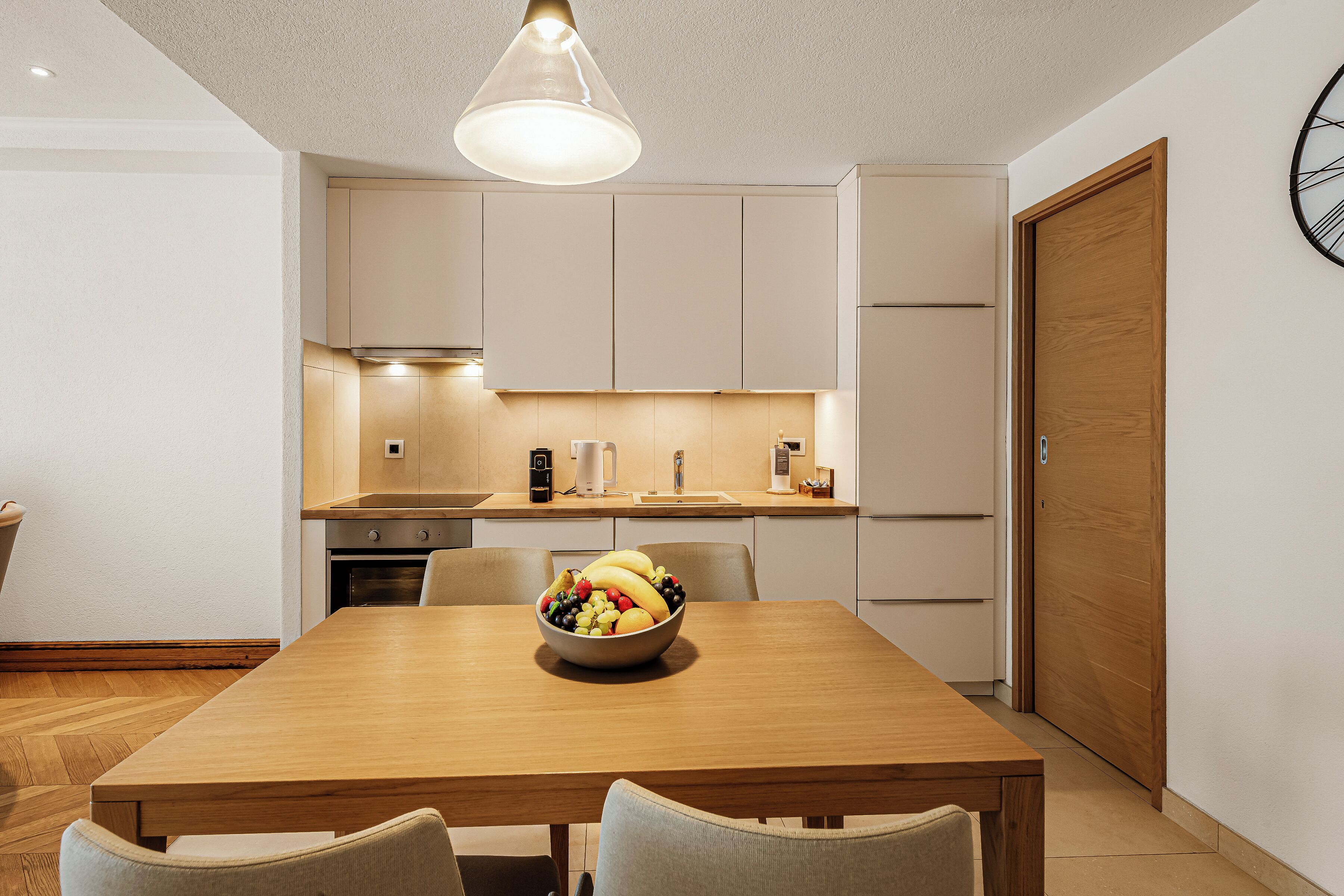 Una cocina moderna con una mesa de comedor de madera, un bol de fruta y un reloj en la pared.