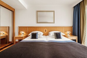 A hotel room with a large bed, wooden headboard, two bedside tables with lamps, and a mirror on the wall. - Villa Malo More (Dubrovnik)
