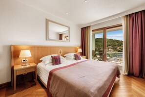 Quarto de hotel com uma cama grande, mesa de cabeceira com luminária, espelho e vista para uma varanda com paisagem deslumbrante.