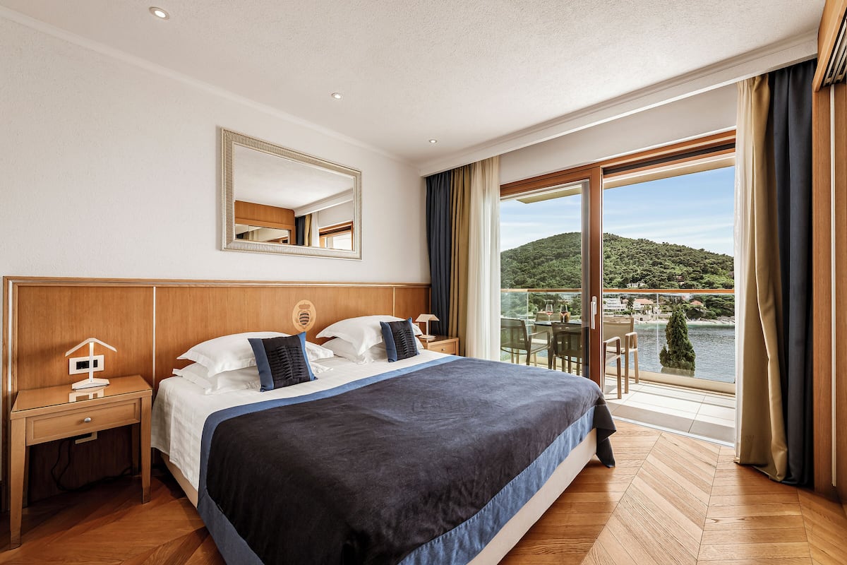 A hotel room with a large bed, a nightstand, a mirror, and a view of a lake and hills.