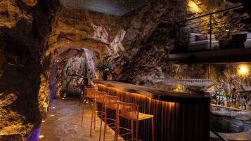 Uma área de bar com balcão de madeira, banquetas e piso de pedra.