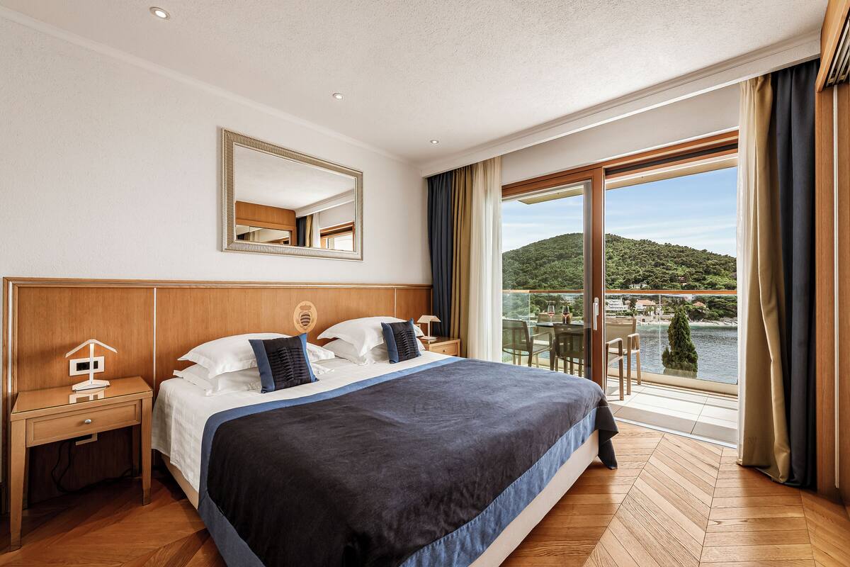 A hotel room with a large bed, a nightstand, a mirror, and a view of a lake and hills.
