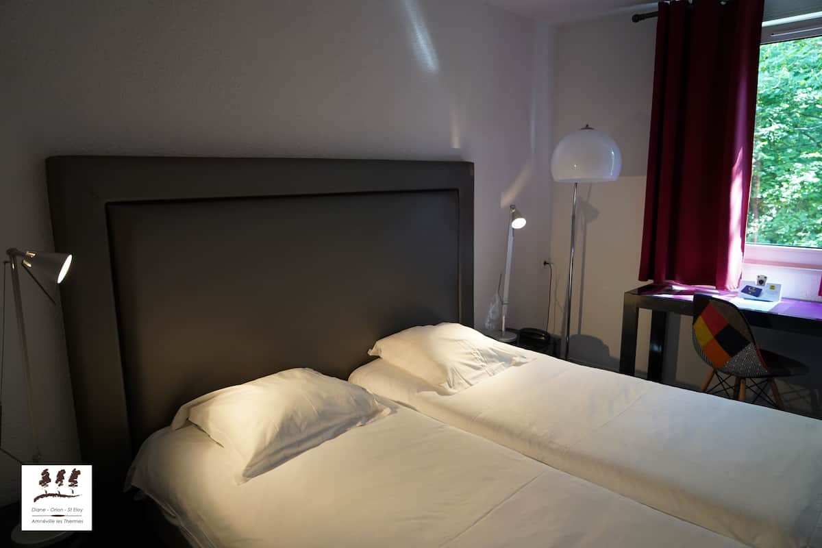 A bedroom with a large bed, a desk, a chair, and a window with curtains.
