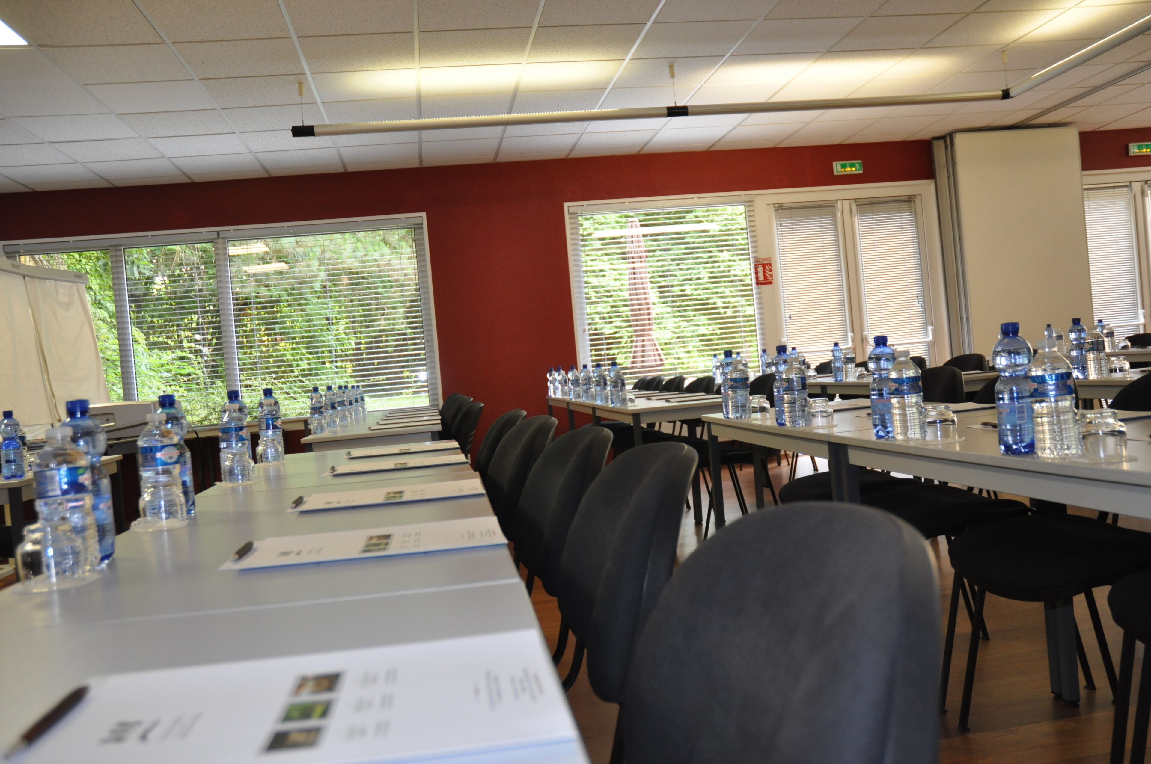 A conference room with long tables, chairs, water bottles, and a projector screen.