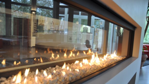 A modern interior with a glass fireplace, wooden flooring, and a view of the outdoors.