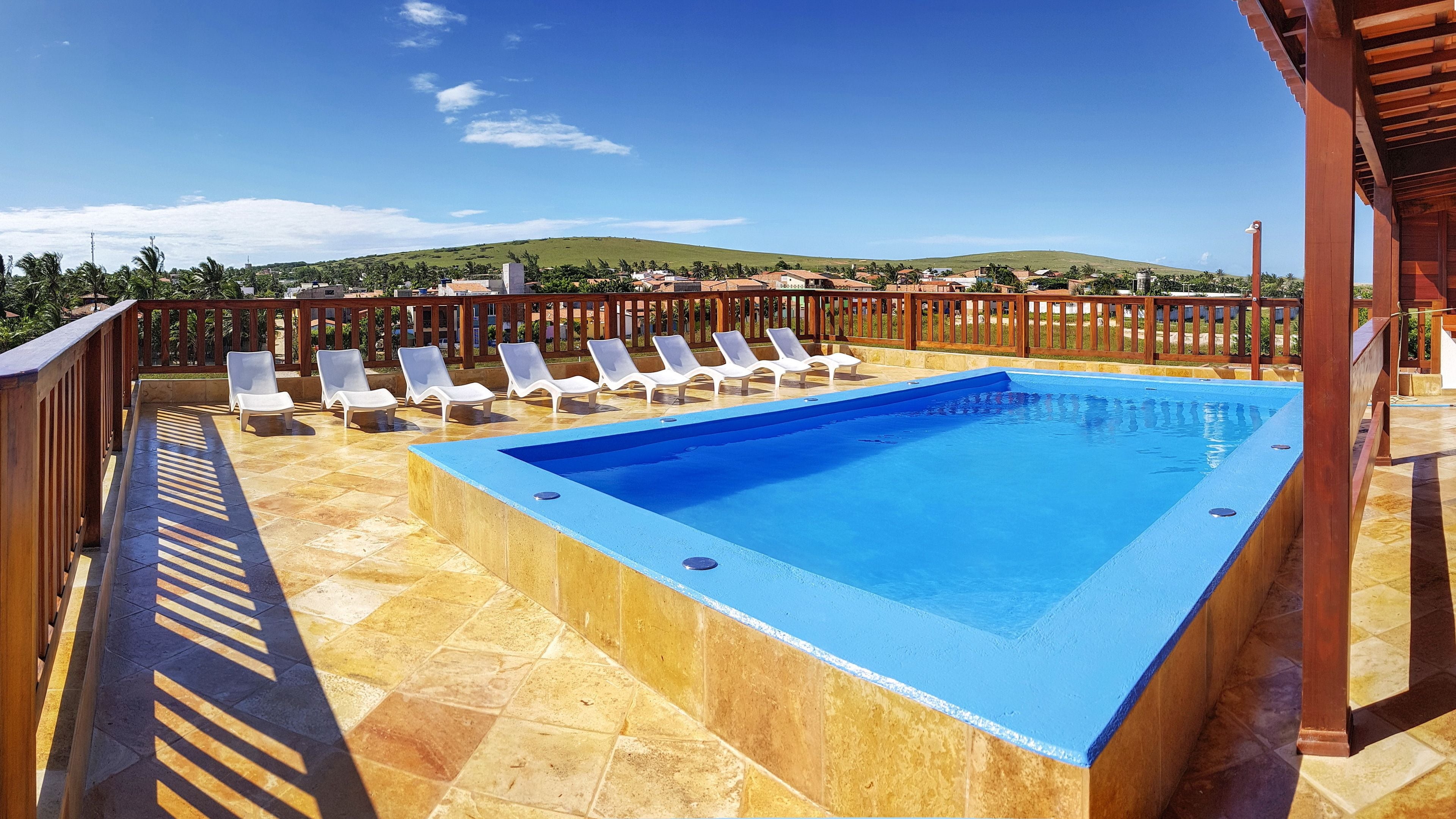 A rectangular swimming pool with a blue interior, surrounded by a wooden deck and white lounge chairs.