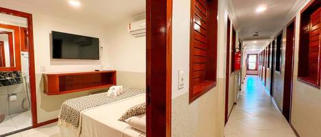 Habitación de hotel con cama, televisor, baño y un pasillo con puertas.