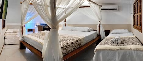 Una habitación con dos camas, cada una con dosel y una manta estampada. Hay un banco y una silla en la esquina.