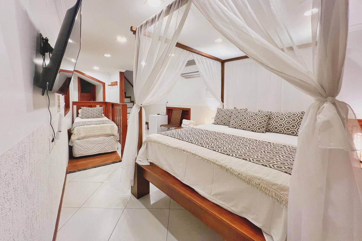 A bedroom with a large bed, a smaller bed, a TV mounted on the wall, and a staircase leading to an upper level.