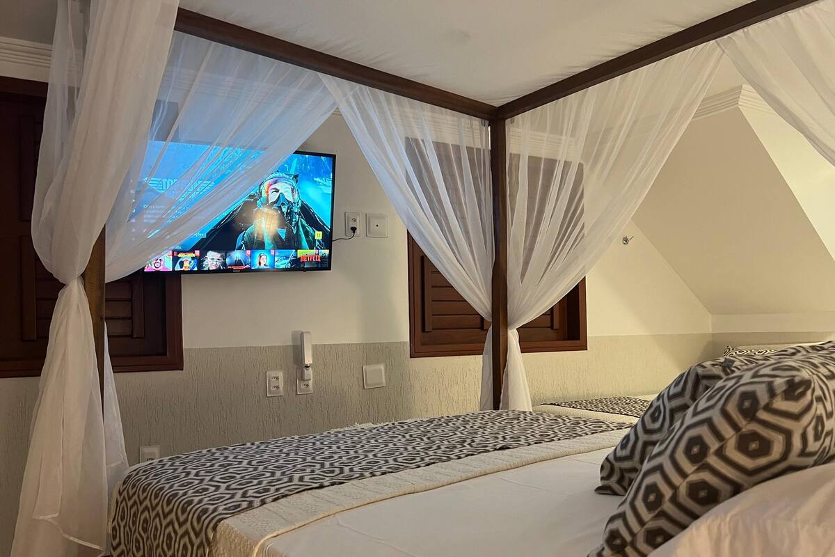 A bedroom with a bed, a TV mounted on the wall, and a window with curtains.