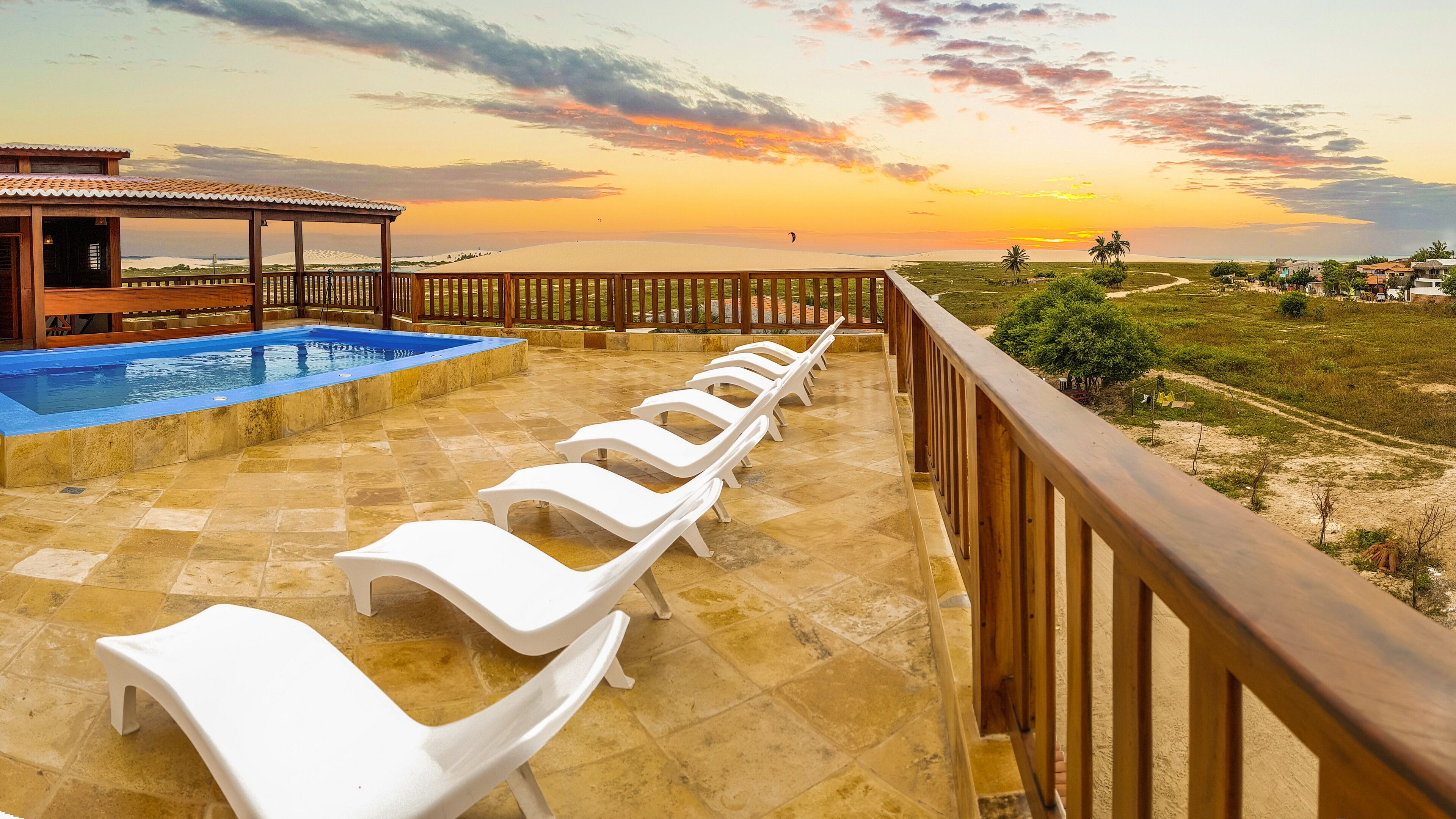 A pool area with lounge chairs and a wooden deck overlooking a scenic landscape during sunset.