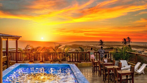 Zona de piscina con vista al atardecer, terraza de madera y sillones de descanso.