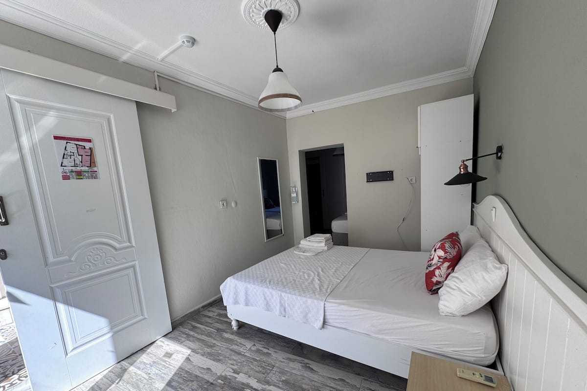 A bedroom with a bed, a bedside table, a mirror, a door, and a light fixture.