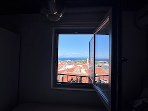 A room with a window overlooking a cityscape with red-roofed buildings and a clear blue sky.