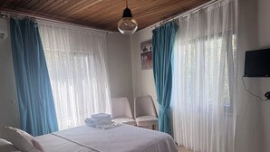 Un dormitorio con cama, una silla, un televisor y cortinas.