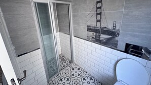 Un baño con cabina de ducha de vidrio, suelo de baldosas con un mural de puente y un inodoro blanco.