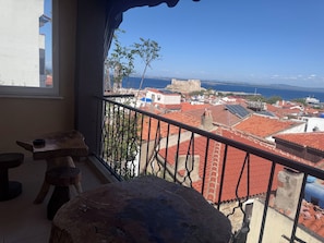 A balcony with a view of a coastal town, including a castle and red-roofed buildings.