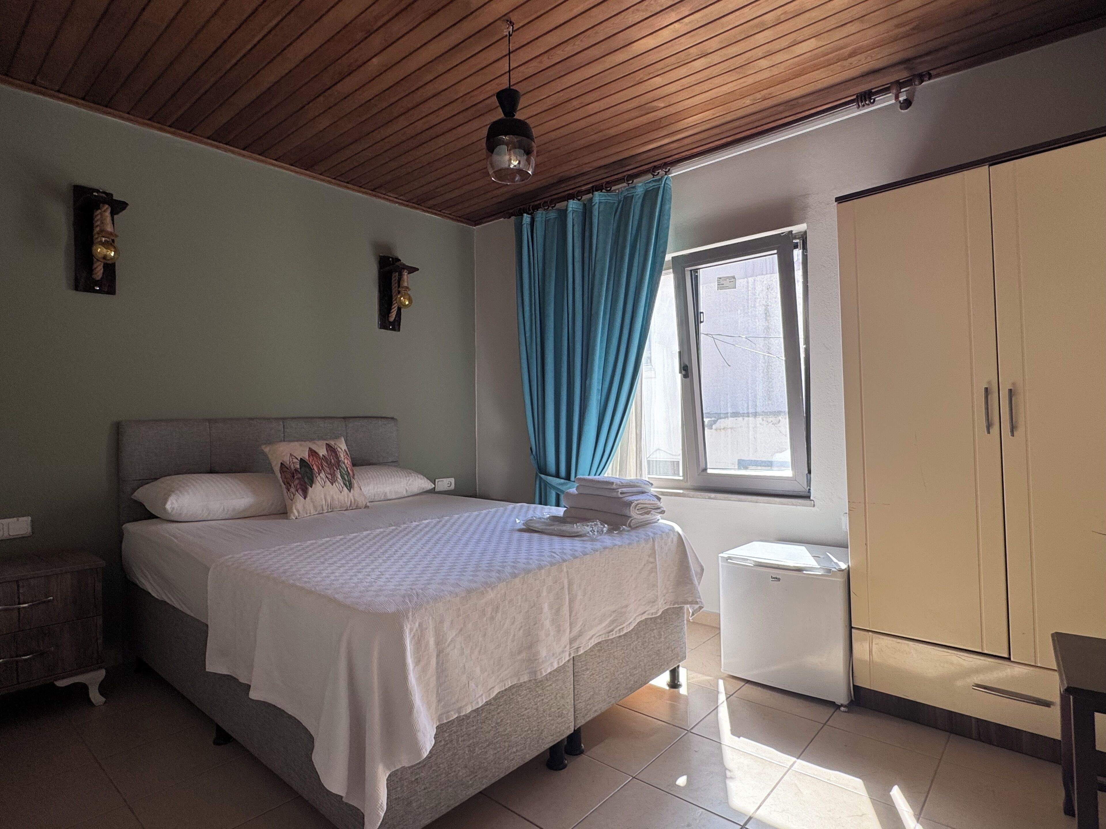 A bedroom with a bed, a wardrobe, a window with curtains, a ceiling fan, and a wall-mounted light fixture.