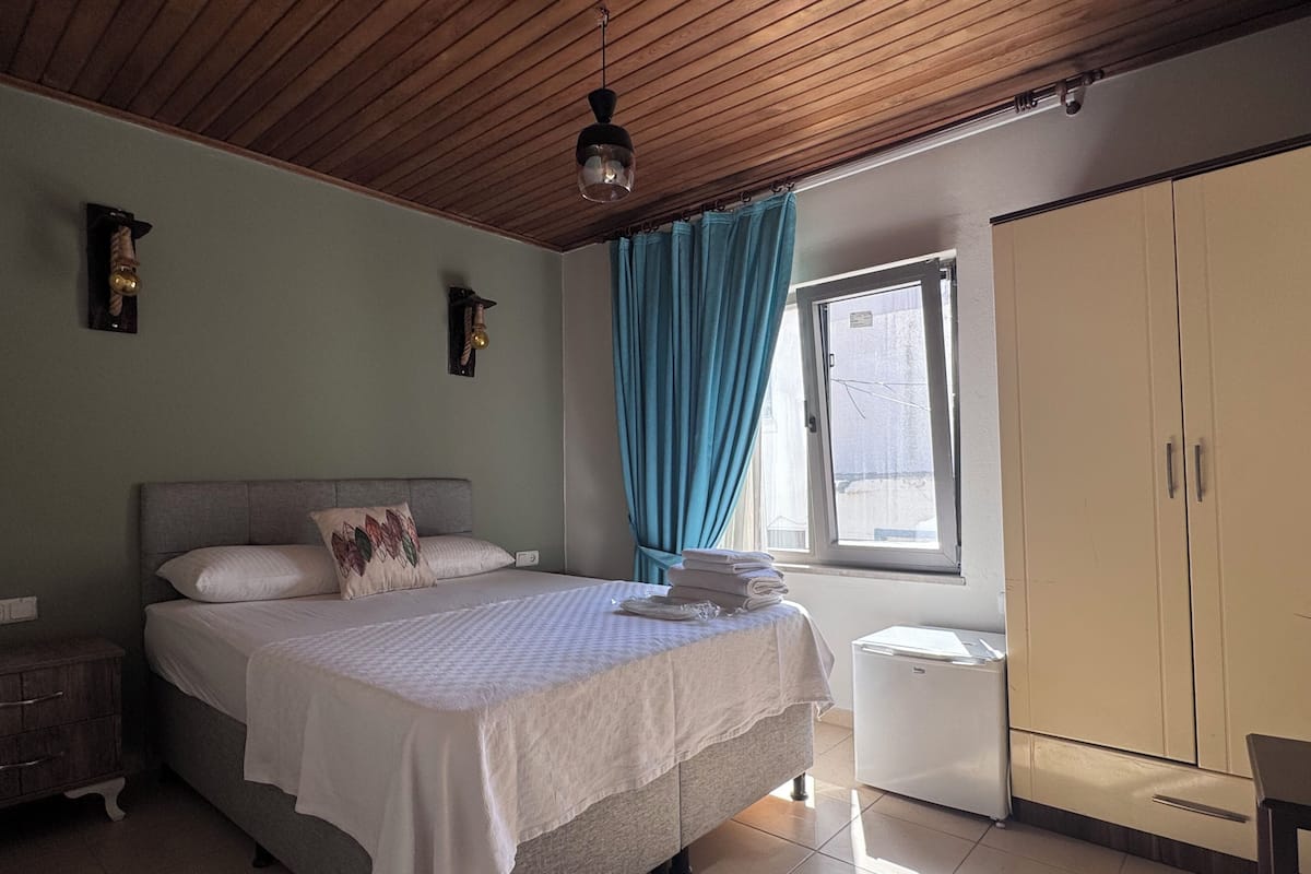 A bedroom with a bed, a wardrobe, a window with curtains, a ceiling fan, and a wall-mounted light fixture.