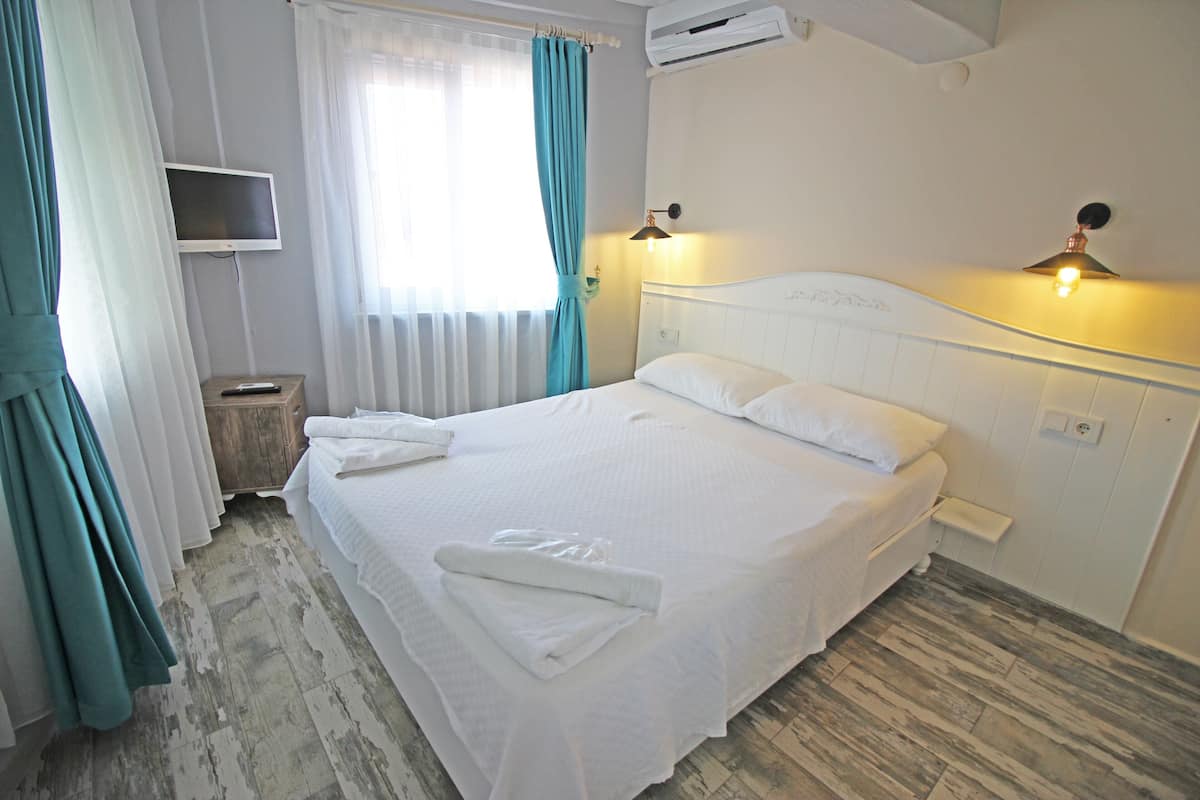 A neatly made bed with white linens, a bedside table with a remote control, a wall-mounted TV, and a ceiling fan.