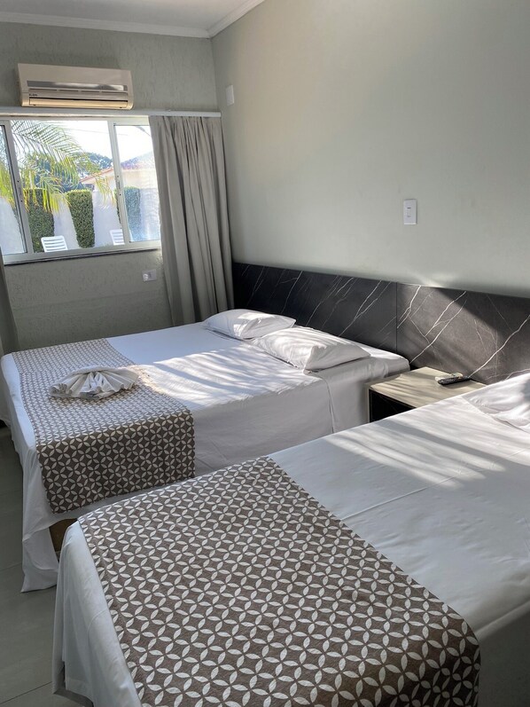 Habitación de hotel con dos camas, cabecera de mármol, equipo de aire acondicionado, ventana con cortinas y vista a zonas verdes.