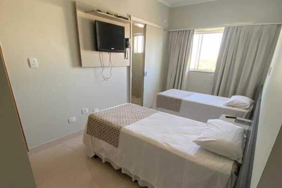 A bedroom with two beds, a TV mounted on the wall, and a window with curtains.