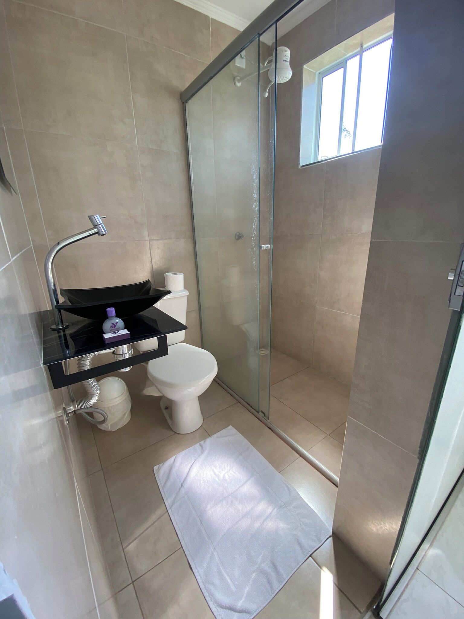 Um banheiro moderno com box de vidro, pia preta com espelho e vaso sanitário branco.
