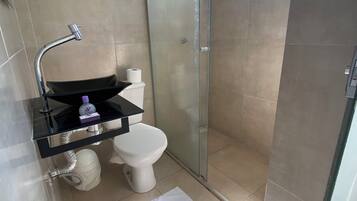 Um banheiro moderno com box de vidro, pia preta com espelho e vaso sanitário branco.
