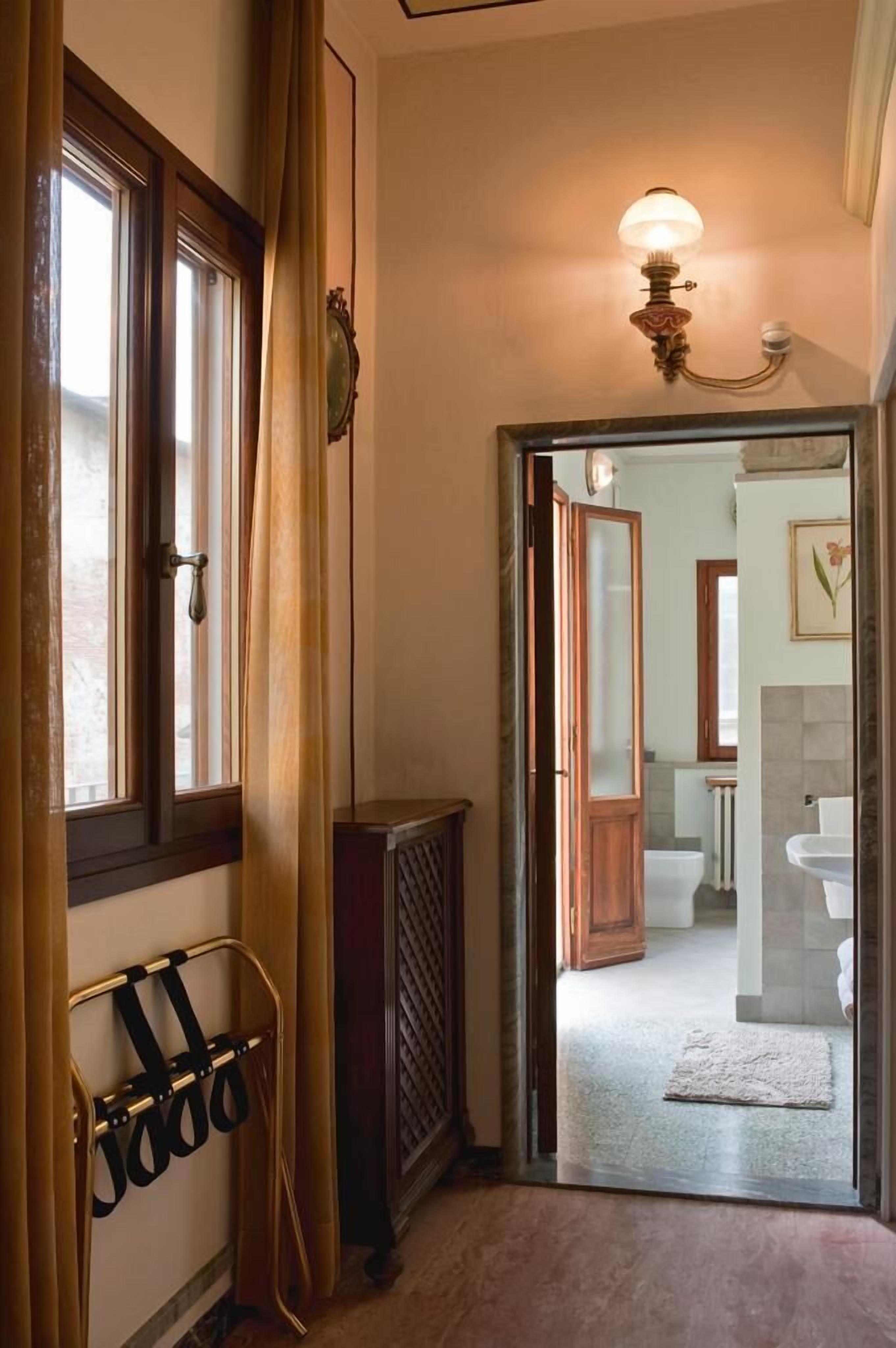 A hallway with a wooden door leading to a bathroom. A coat rack with hanging items is visible on the left.