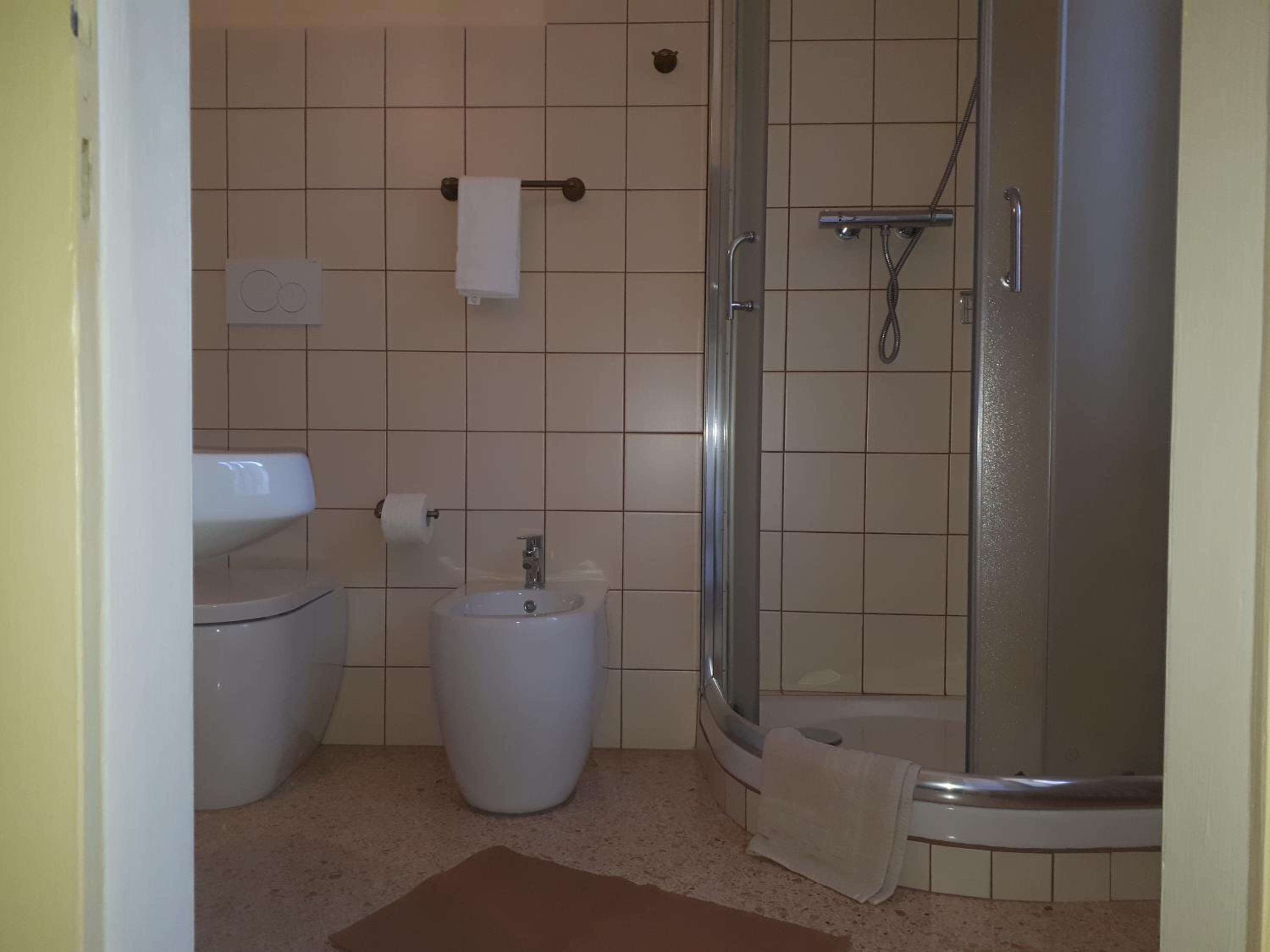 A bathroom with a toilet, sink, bidet, and a glass-enclosed shower.