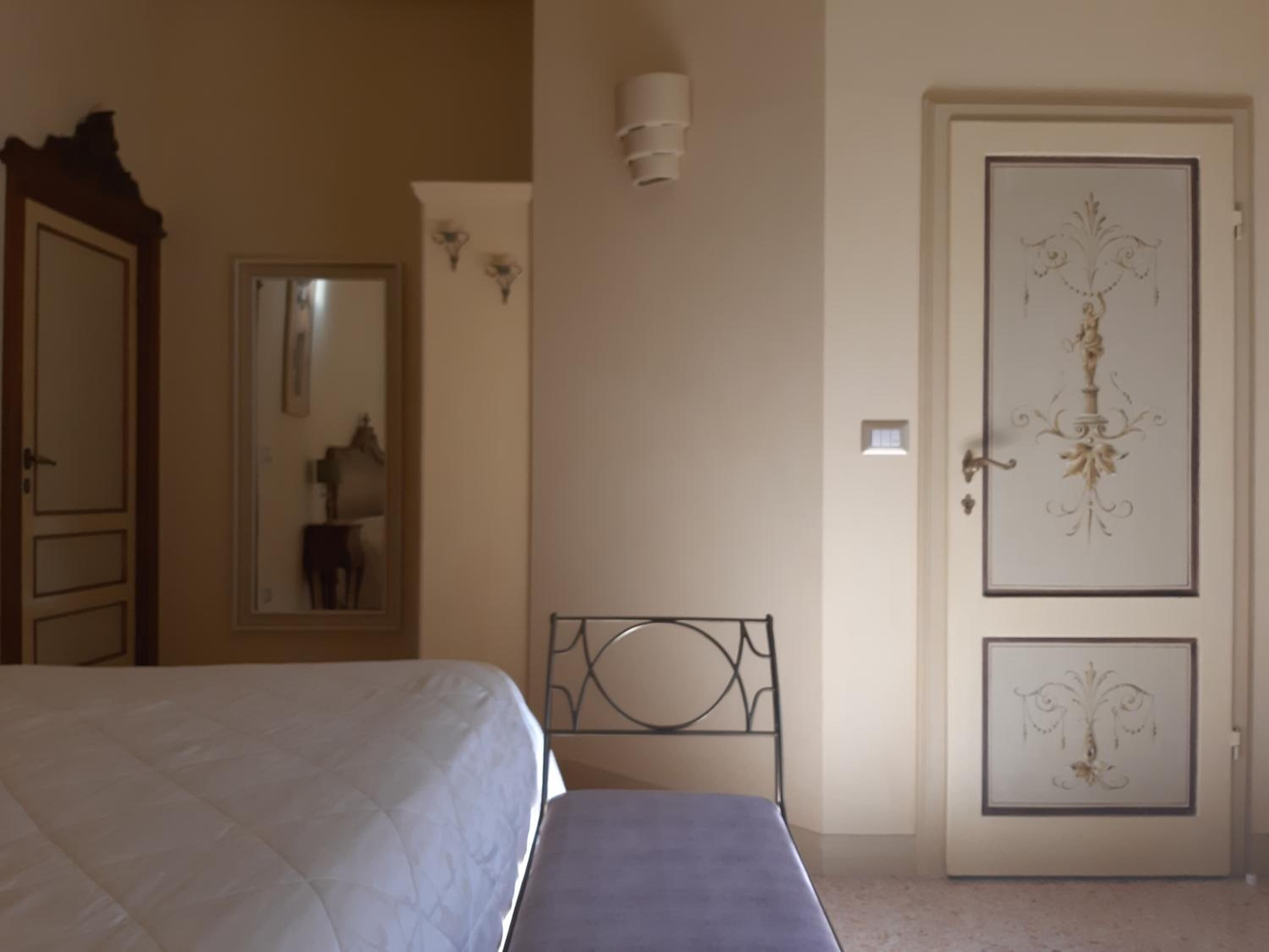 Quarto com cama, mesa de cabeceira, espelho e porta com detalhes decorativos.