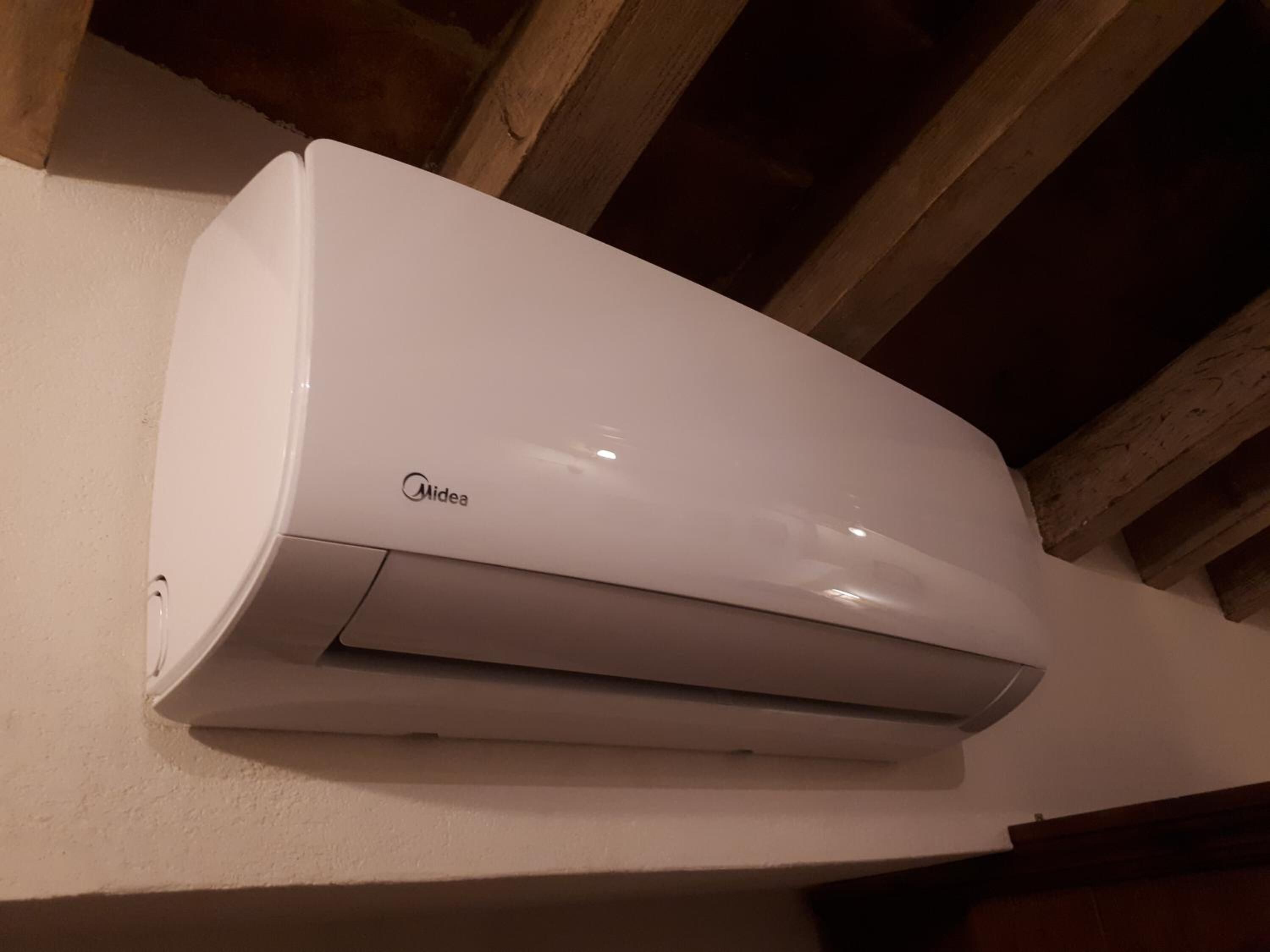 Een witte Midea airconditioner hangt aan een muur met houten balken erboven.