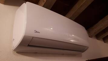 Een witte Midea airconditioner hangt aan een muur met houten balken erboven.