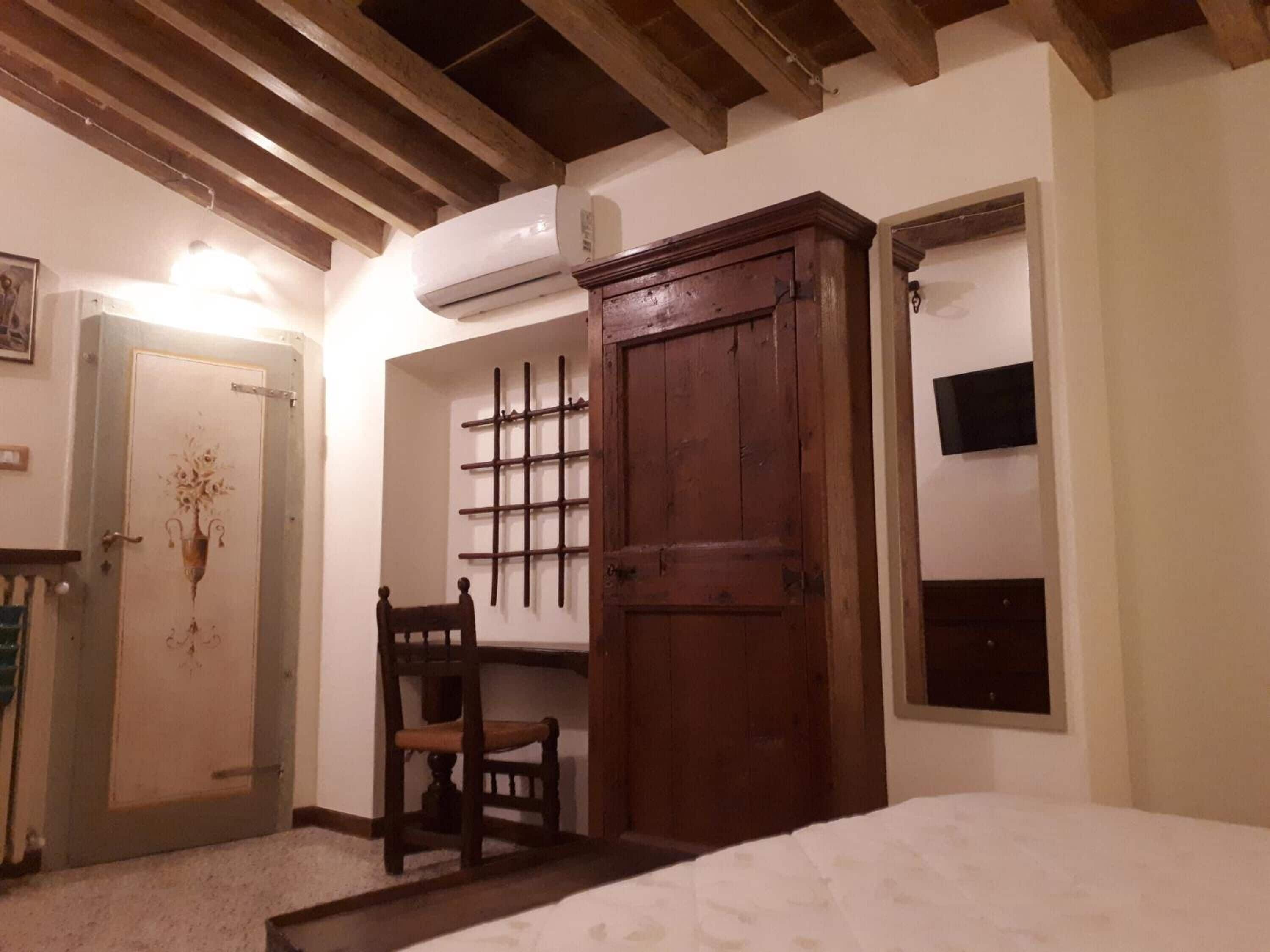 A room with a bed, a wooden wardrobe, a chair, a wall-mounted shelf, and a door with a decorative design.