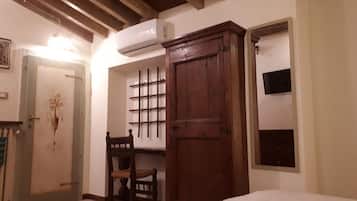 A room with a bed, a wooden wardrobe, a chair, a wall-mounted shelf, and a door with a decorative design.