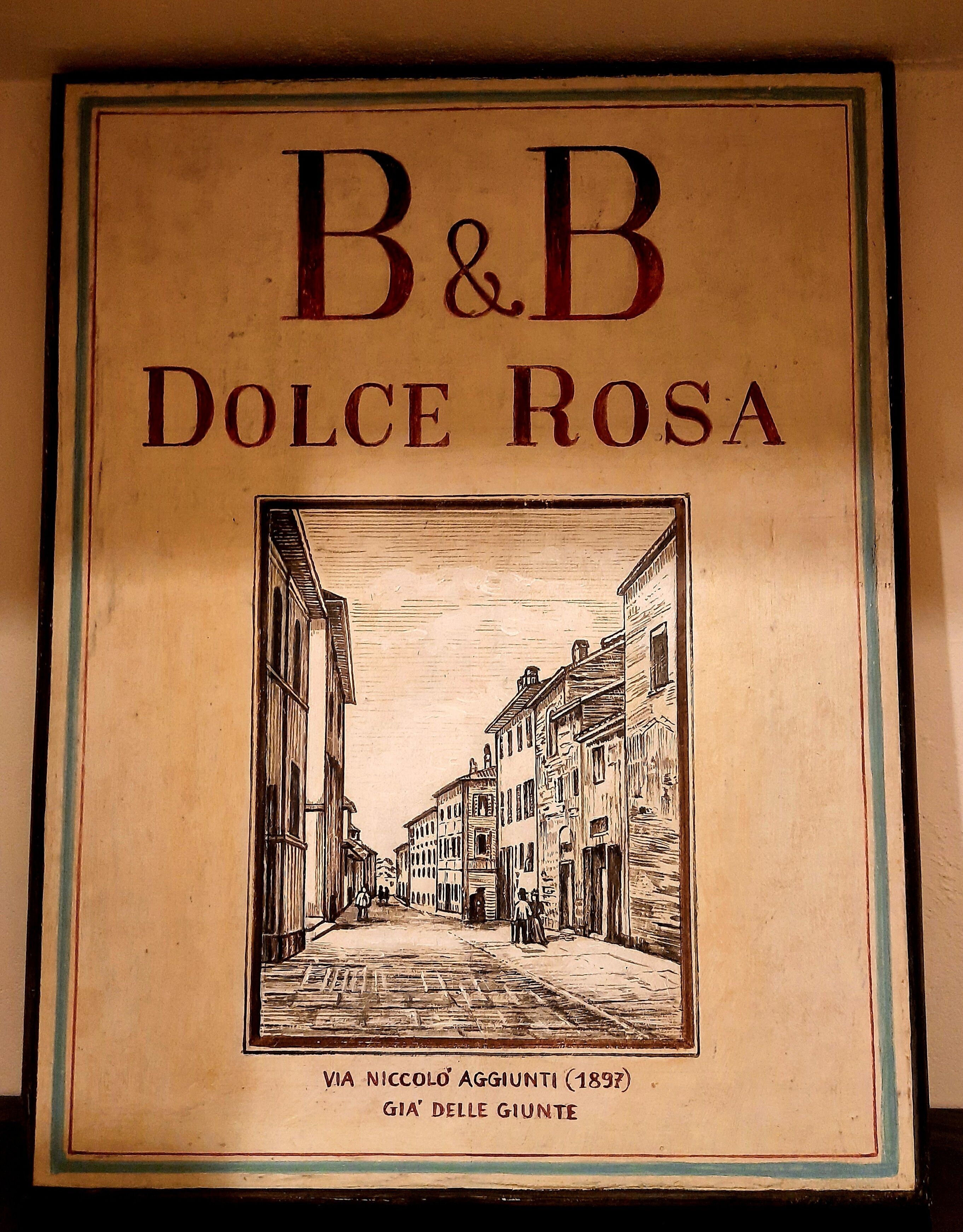 Uma placa emoldurada com 'B&B Dolce Rosa' e uma ilustração de uma cena de rua.