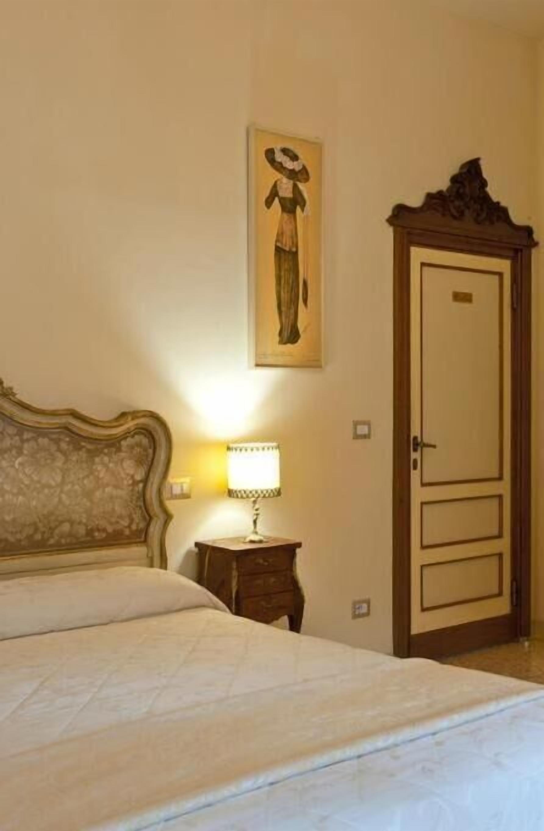 A bedroom with a bed, a nightstand with a lamp, a wardrobe, and a framed picture on the wall.