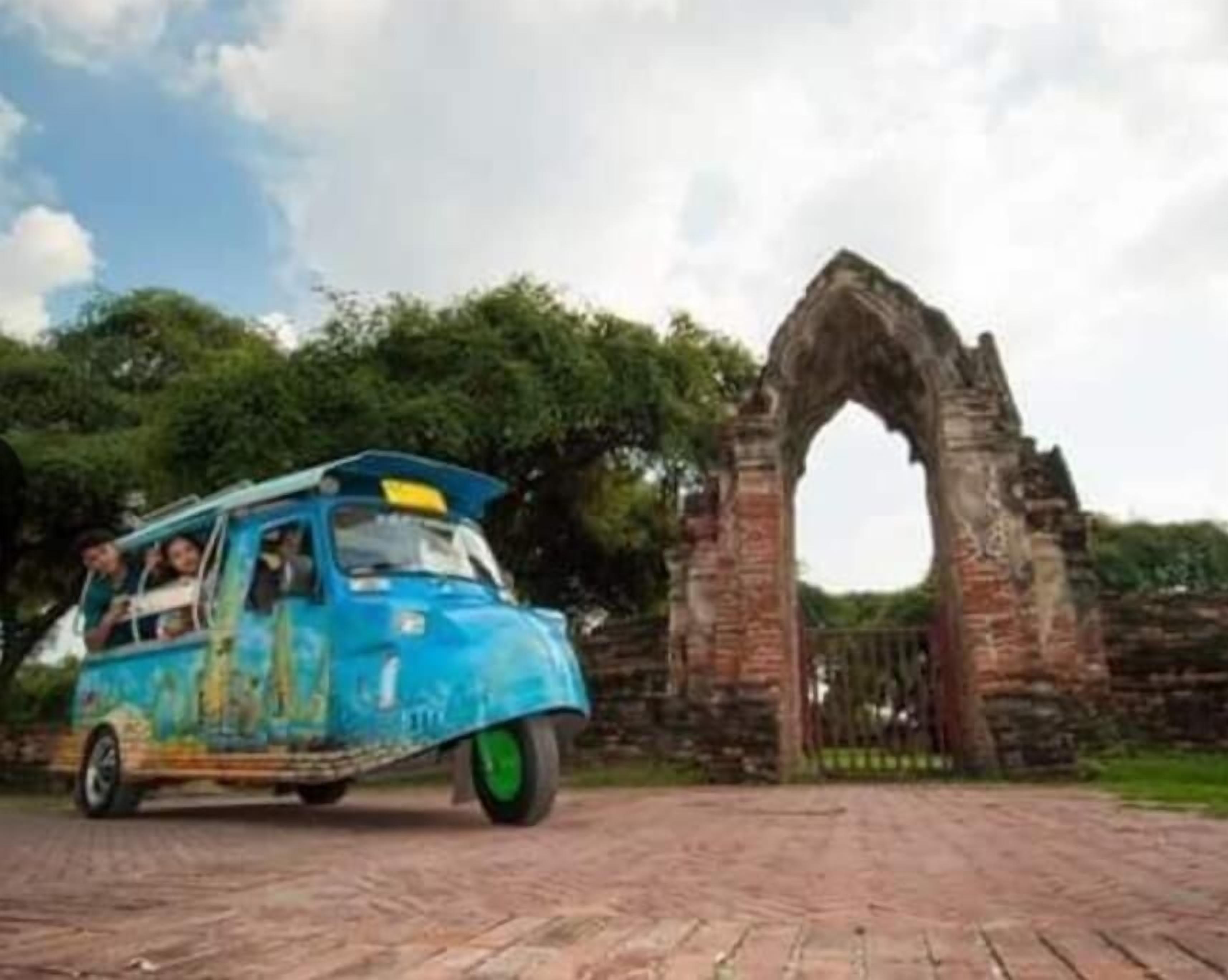Un véhicule bleu transportant des passagers, garé devant un ancien arc en pierre.