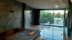 A modern room with a large window, a bed with a blanket and pillows, and a wooden floor. - Lom Choi Home Stay Ayutthaya - Hostel (Ayutthaya)