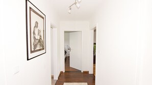 A hallway with a framed artwork on the left, a white door at the end, and a wooden floor. - Ferienwohnung BECKENDORF 3 (Losheim am See)