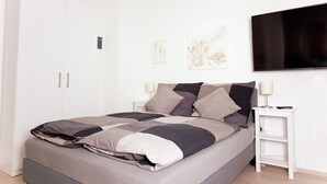 A modern bedroom with a large bed, white nightstands, and a flat-screen TV. - Ferienwohnung BECKENDORF 3 (Losheim am See)