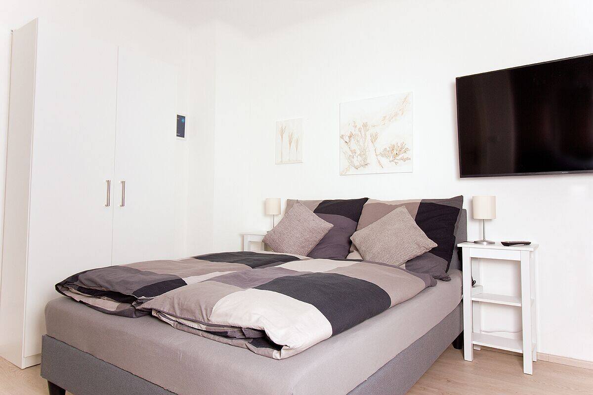 A modern bedroom with a large bed, white nightstands, and a flat-screen TV.
