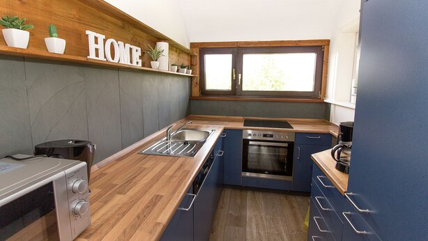 A compact kitchen with a wooden countertop, a built-in oven, a sink, and a window above the sink. - Ferienwohnung BECKENDORF 3 (Losheim am See)