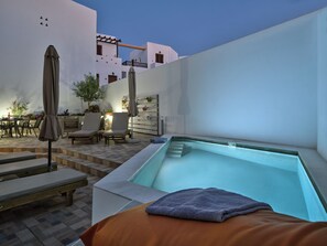 Un área de piscina en la azotea con sillones, un jacuzzi y una pérgola.